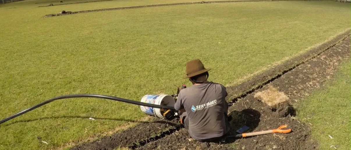 Técnico de SERVIMED instalando la cañería de riego automatizado en una cancha de césped